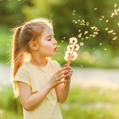 Child outside blowing dandelions