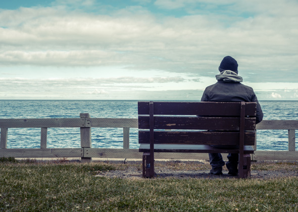 man sat on a bench looking out to sea