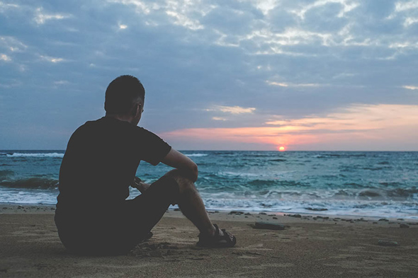 Man sitting on sand by beach at sunset